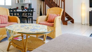 A living room with wicker furniture, a glass coffee table, and a wooden staircase. - Air-conditioned 4-Room Villa with WIFI, Terrace, BBQ, and Parking - Sleeps 6 (Narbonne)