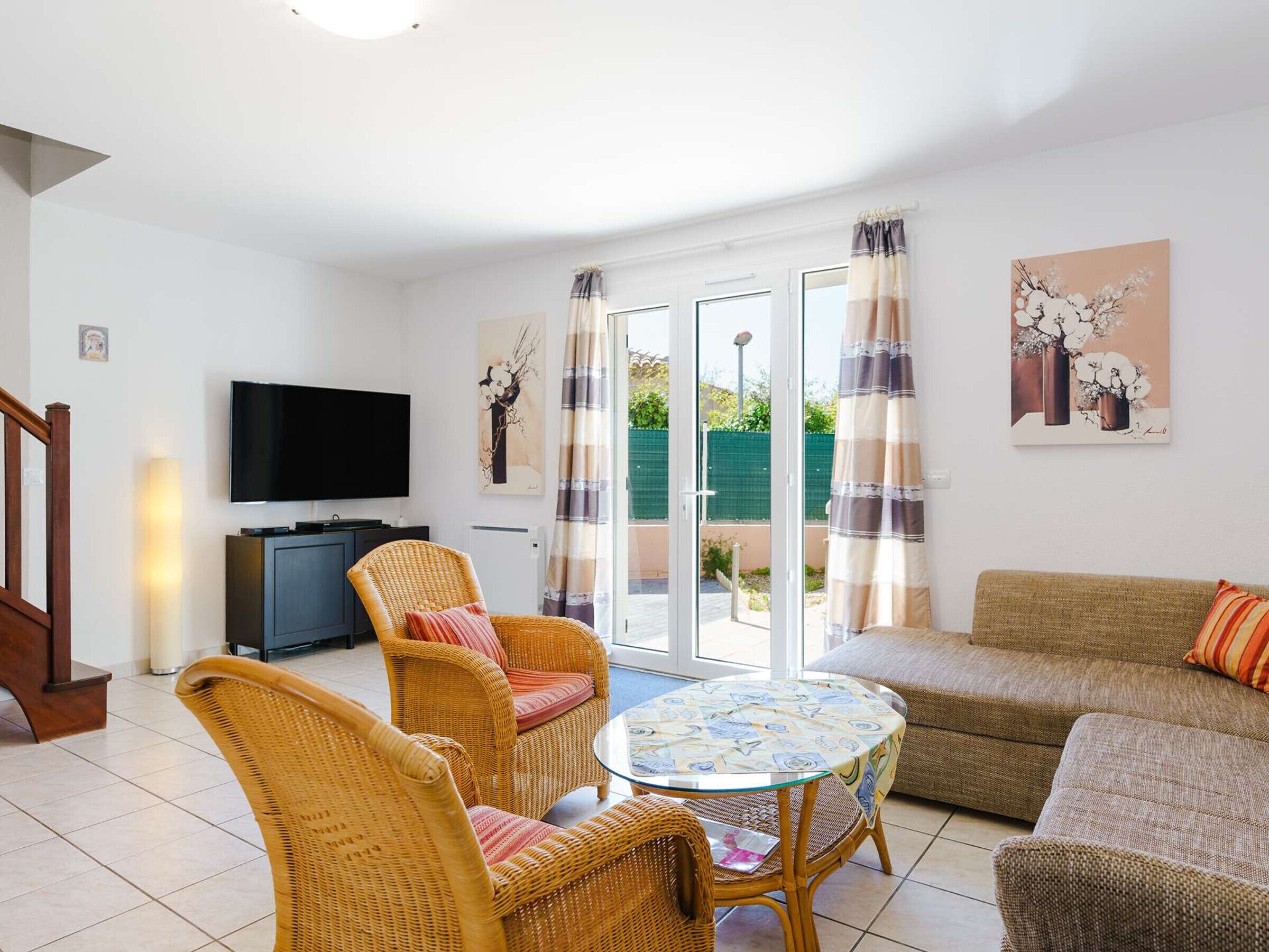 A living room with a television, wicker furniture, a glass table, and a sofa.