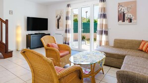 A living room with a television, wicker furniture, a glass table, and a sofa. - Air-conditioned 4-Room Villa with WIFI, Terrace, BBQ, and Parking - Sleeps 6 (Narbonne)
