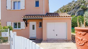 A two-story building with a white door and garage, surrounded by a white fence and potted plants. - Air-conditioned 4-Room Villa with WIFI, Terrace, BBQ, and Parking - Sleeps 6 (Narbonne)