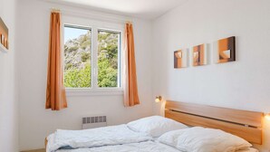 A bedroom with a wooden bed, white bedding, a window with curtains, and three wall-mounted artworks. - Air-conditioned 4-Room Villa with WIFI, Terrace, BBQ, and Parking - Sleeps 6 (Narbonne)
