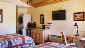 A cozy room with two beds, a washing machine, a microwave, a TV, and a desk with a chair.