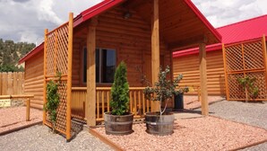 A wooden cabin with a red roof, a porch with a railing, and two potted plants.