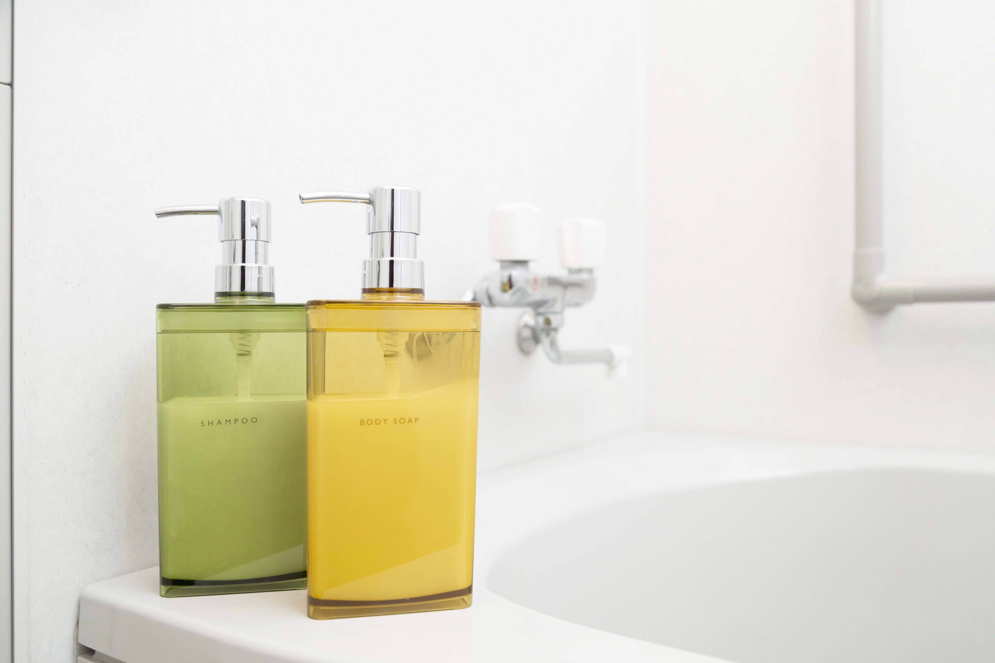 Two bottles of shampoo and body soap on a white countertop next to a white bathtub.