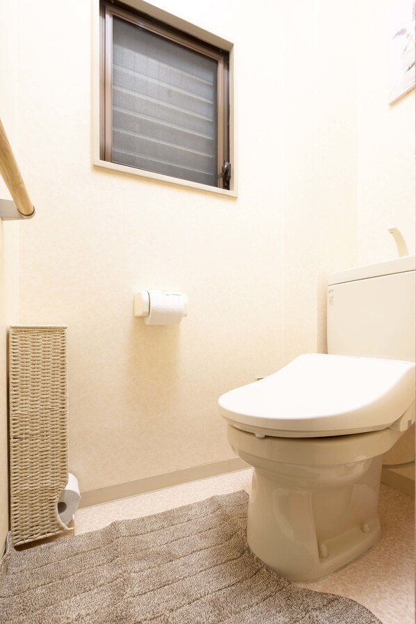 A bathroom with a toilet, a roll of toilet paper, a towel rack, and a window.