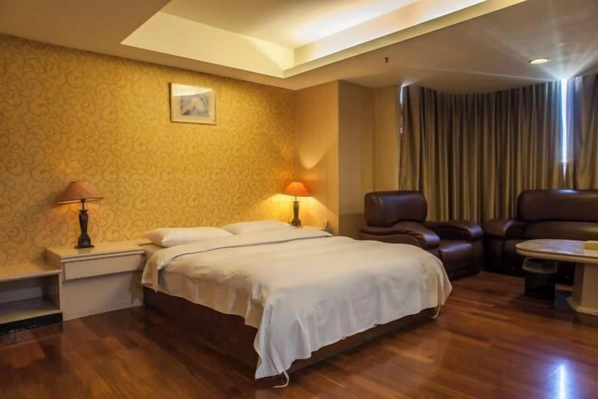 Habitación de hotel con cama, dos sillas, una mesita, una mesita de noche, una lámpara y una cortina.