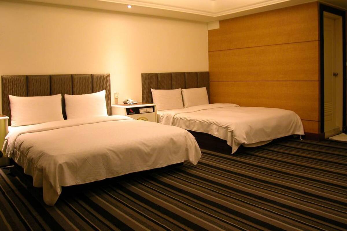 Habitación de hotel con dos camas, una mesita de noche y un panel de pared de madera.