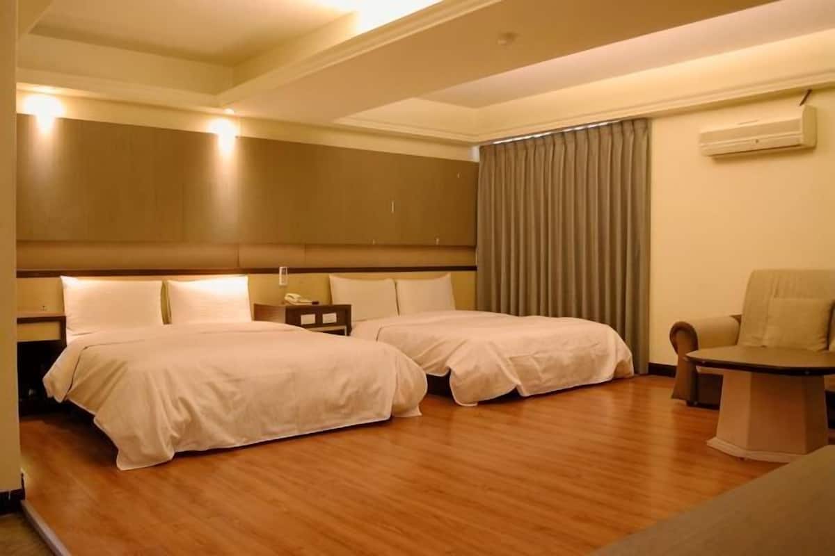Habitación de hotel con dos camas, un escritorio, una silla, una mesita de noche y un ventanal con cortinas.