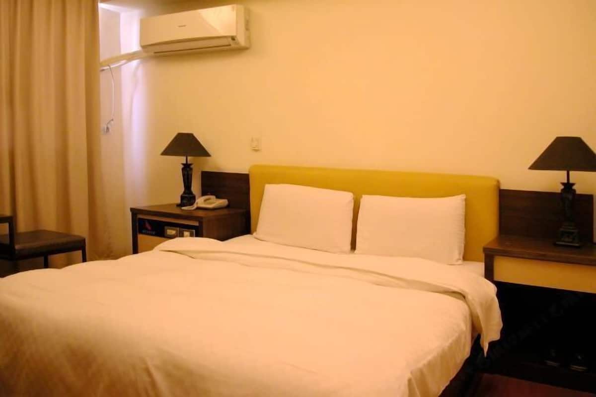 Habitación de hotel con una cama grande, dos mesitas de noche con lámparas, un teléfono y un equipo de aire acondicionado en la pared.