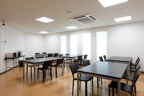 A conference room with multiple tables and chairs, white walls, and large windows.