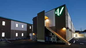 En modern byggnad med en framträdande logotyp i form av ett stort "V", en trappa som leder till entrén och flera utomhusenheter för luftkonditionering.