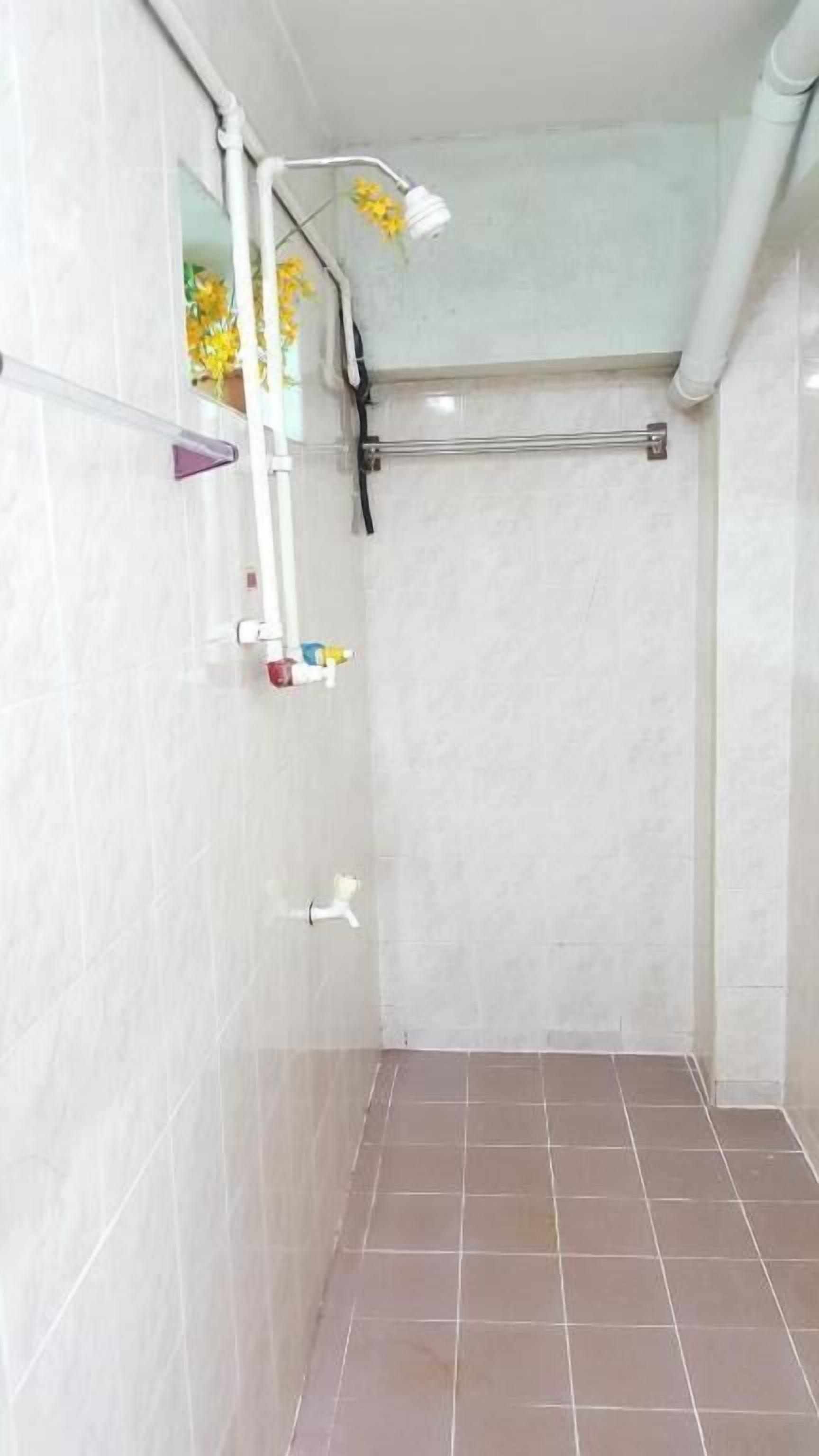 Un baño con paredes de azulejos blancos, una ducha con cabezal de ducha manual y un toallero visible.