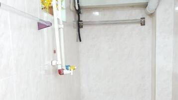 Un baño con paredes de azulejos blancos, una ducha con cabezal de ducha manual y un toallero visible.