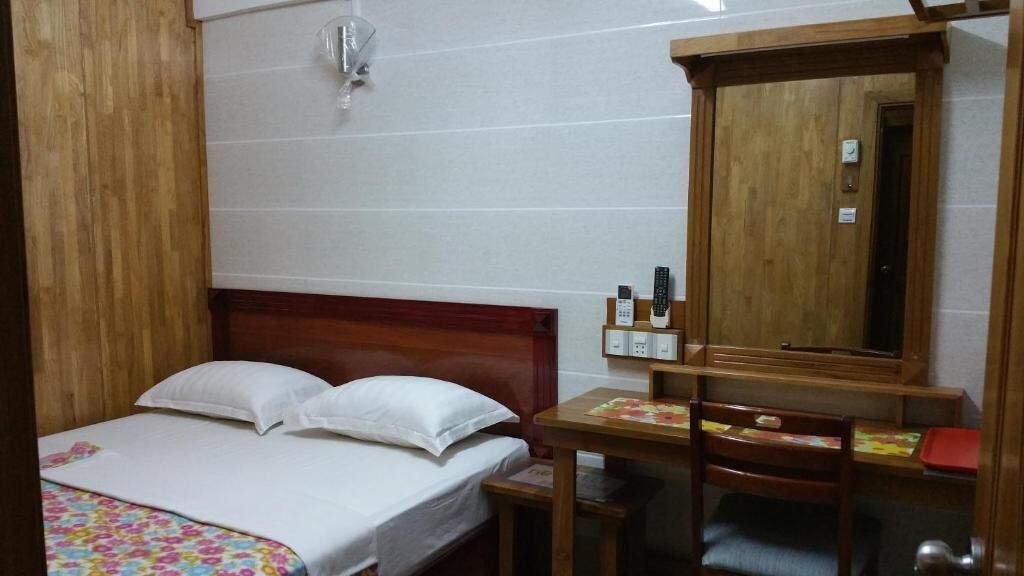 Une chambre à coucher comprenant un lit, un bureau en bois, une chaise, un miroir et un luminaire fixé au mur.