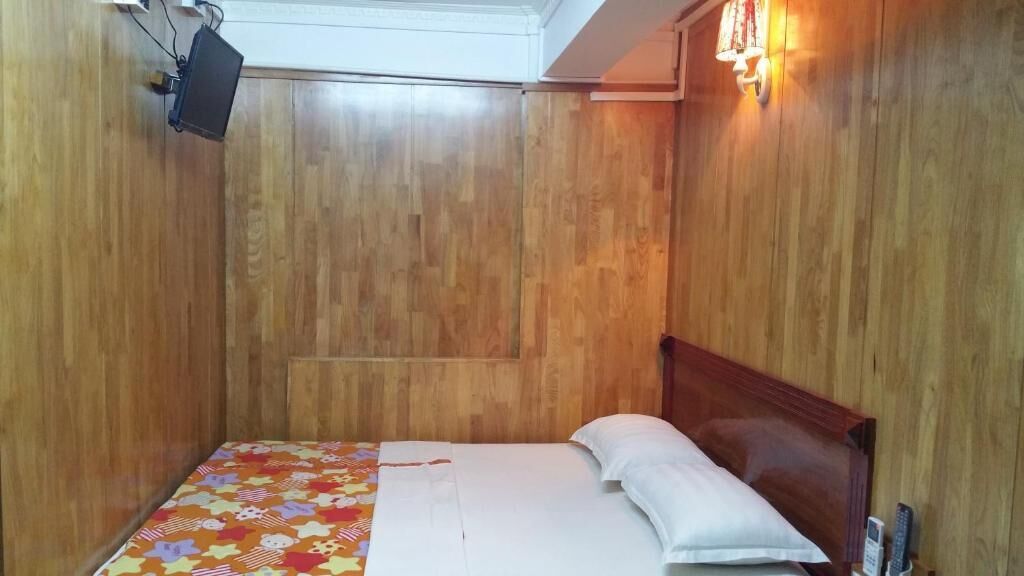 Una stanza con pareti in legno, un letto con biancheria da letto bianca e una coperta colorata, e un televisore a parete.