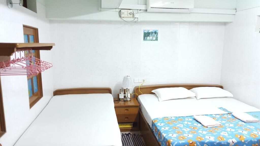 Una habitación de hotel con dos camas individuales, una mesita de noche pequeña con lámpara, aire acondicionado en la pared y una ventana con vistas.