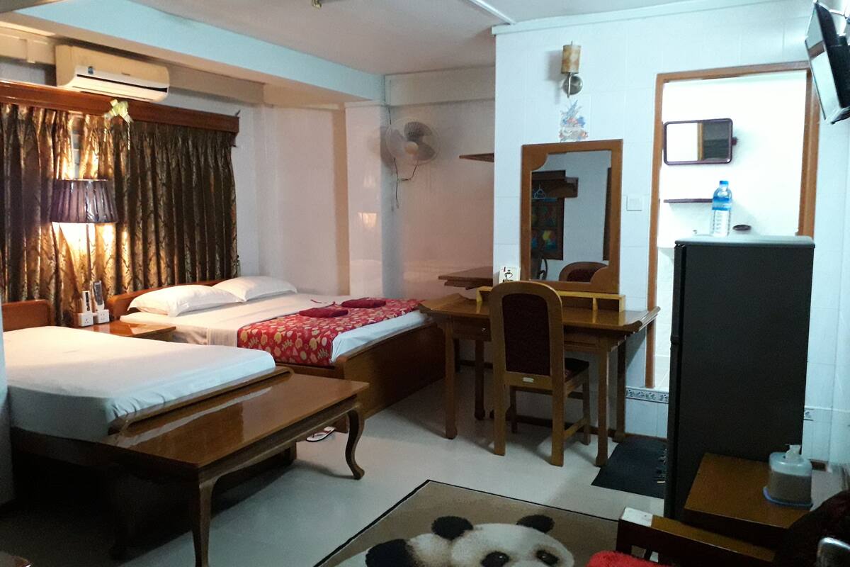A hotel room with two beds, a desk, a chair, a mirror, a television, and a panda plush toy on the floor.