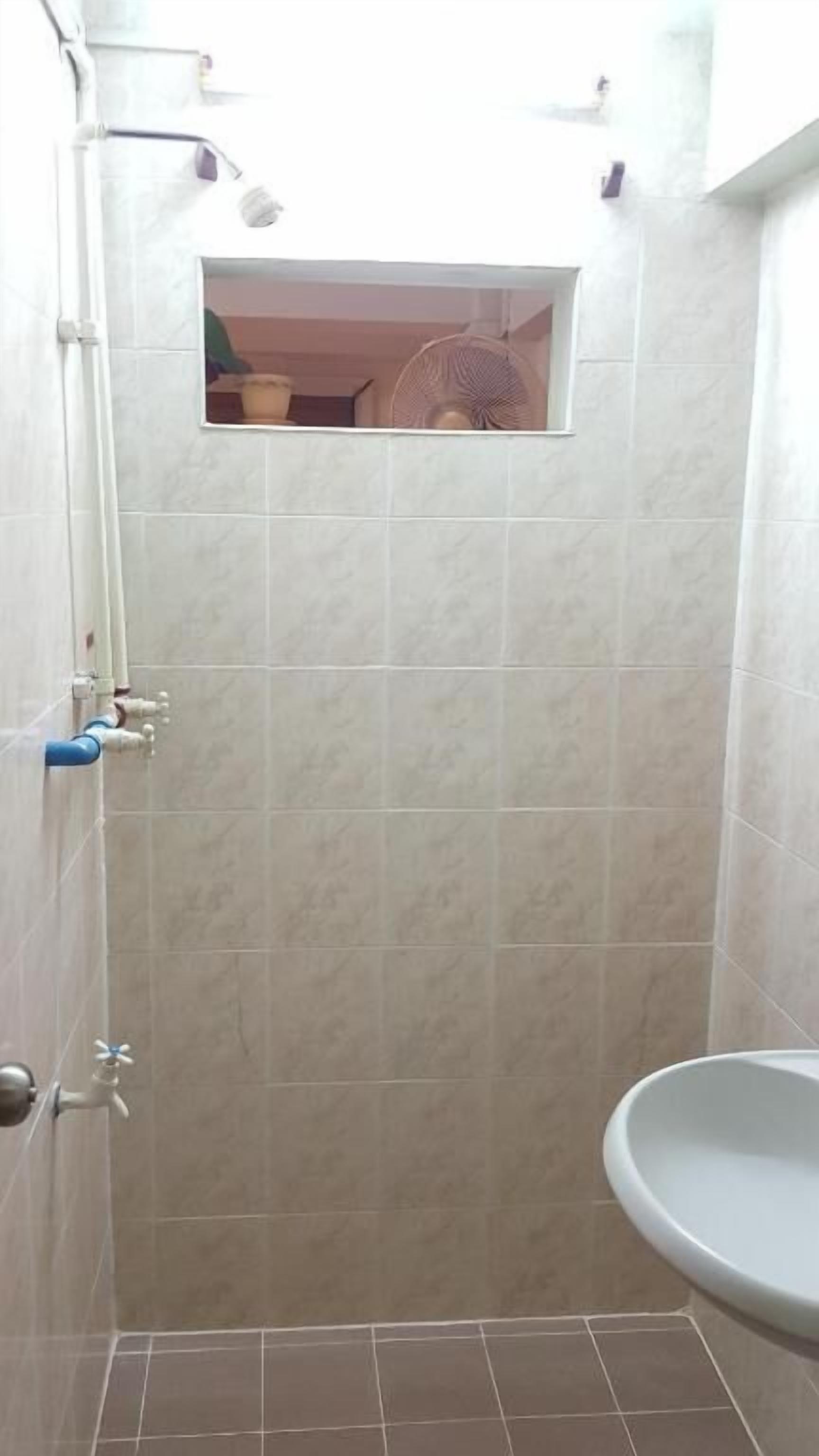 Un baño con ducha, lavabo y un ventanal pequeño.