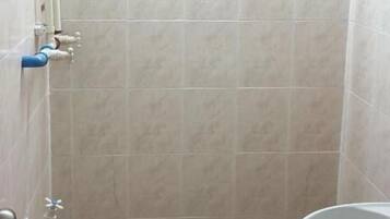 Un baño con ducha, lavabo y un ventanal pequeño.