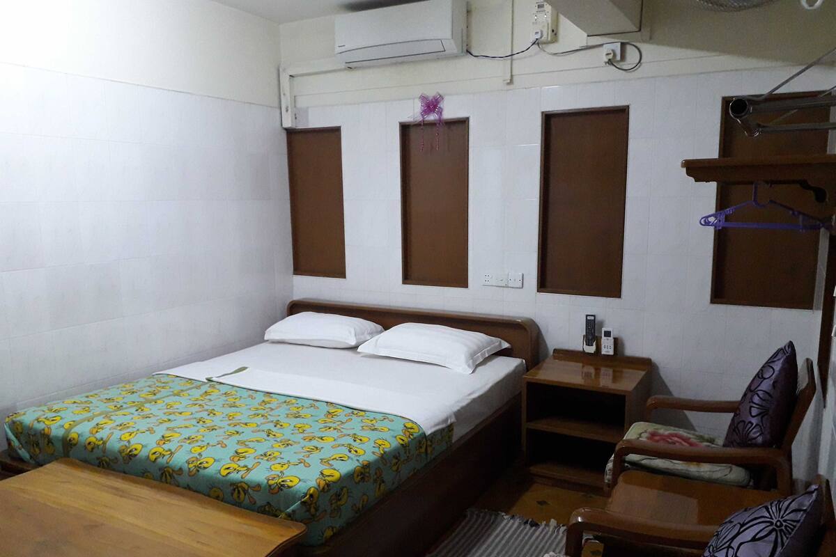 A small, compact hotel room with a single bed, a wooden nightstand, a chair, and a small table.