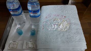 Una bandeja con dos botellas de agua Alpina, dos pequeñas botellas de líquido azul, una toalla blanca con bordado de cisne y dos pequeñas bolsitas con la etiqueta 'LONDON Beauty Soap'.
