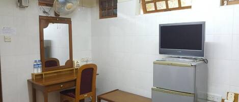 A compact room with a wooden desk, a chair, a small table, a refrigerator, a television, and a window with a view.