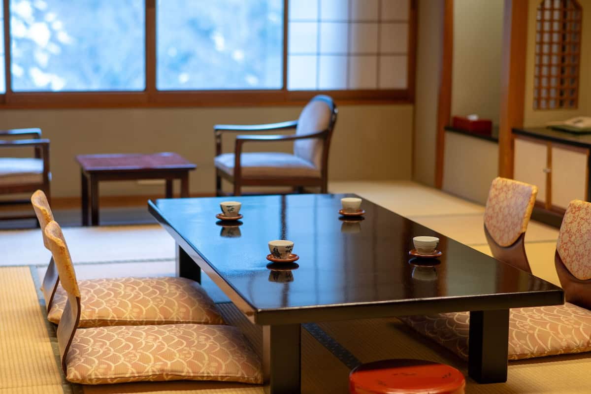 Una habitación tradicional japonesa con suelo de tatami, una mesa baja con cojines y puertas correderas.