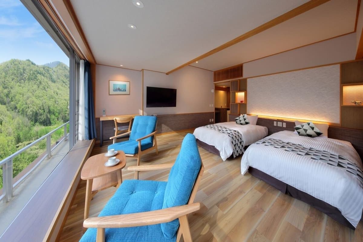 A modern hotel room with a balcony, two beds, a TV, and a dining area.