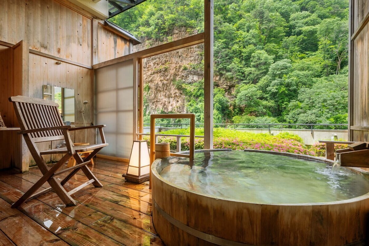A wooden spa with a hot tub, wooden deck, and a view of lush greenery.