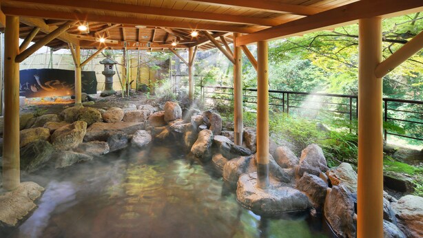 Ein traditionelles japanisches Onsen mit Holzbauten, einem steinernen Pfad und Blick auf üppige Vegetation.