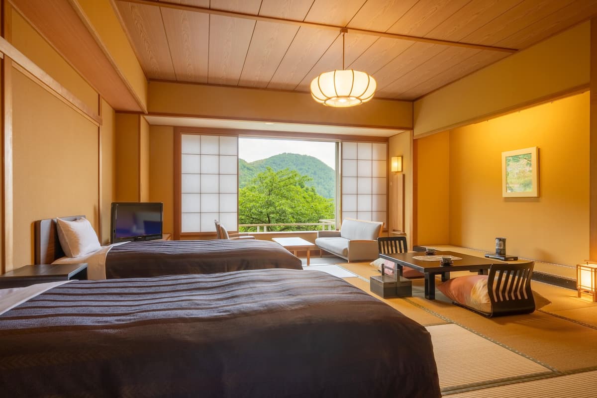 A hotel room with two beds, a TV, a dining table, and a view of a mountain.