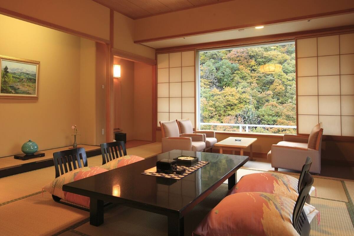 A traditional Japanese room with tatami flooring, a low table, and a view of a forest through a shoji screen.