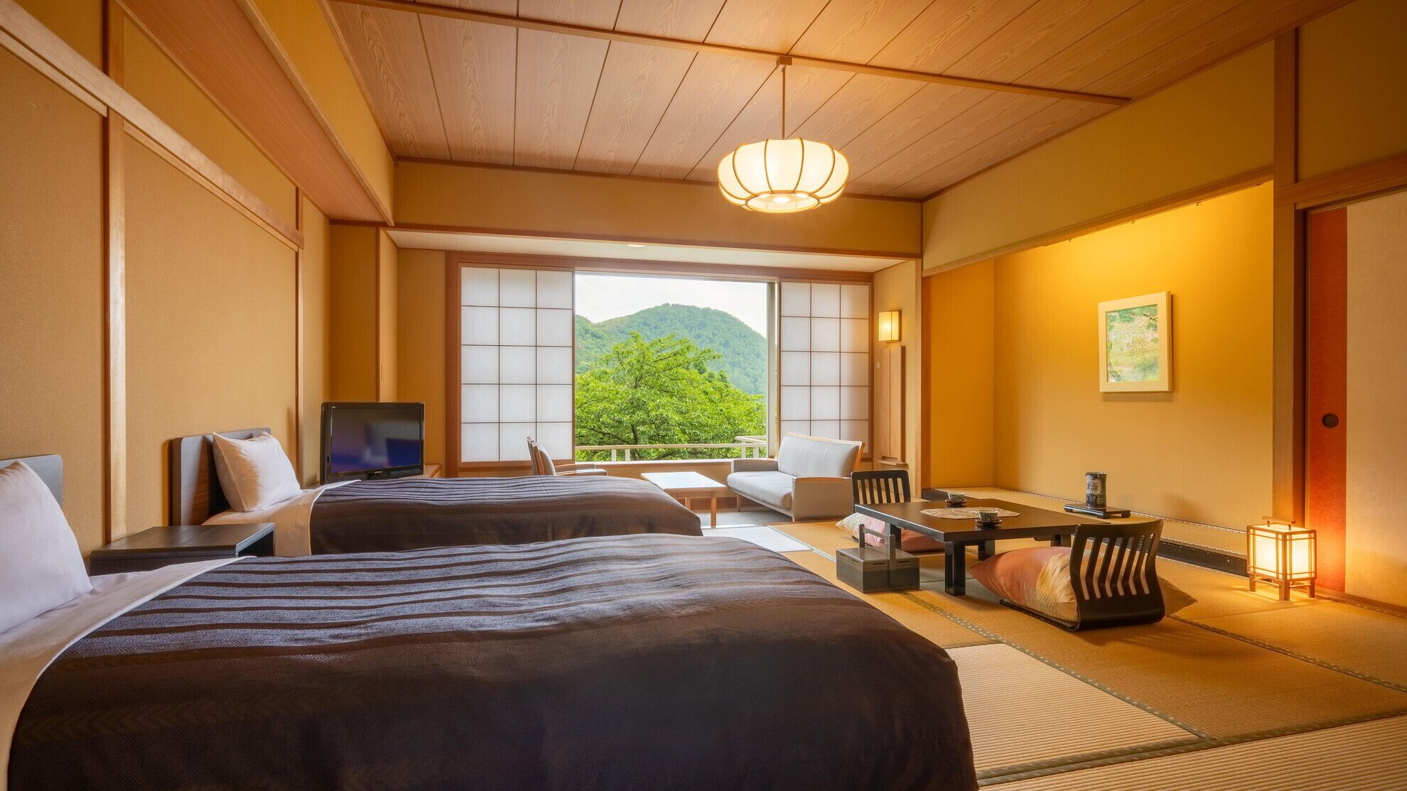 A hotel room with two beds, a television, a dining area, and a view of a mountain.