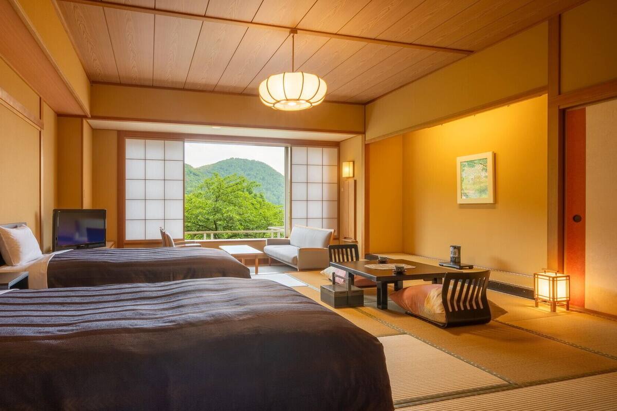 A hotel room with two beds, a television, a dining area, and a view of a mountain.