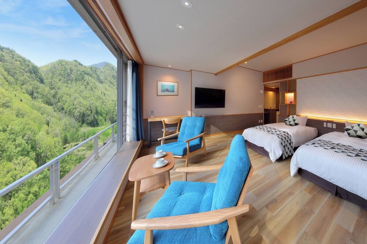 A hotel room with a balcony, two beds, a sofa, a chair, a TV, and a painting.