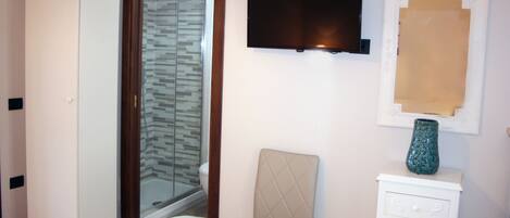 Un baño con ducha, inodoro y tocador con televisor y elementos decorativos.
