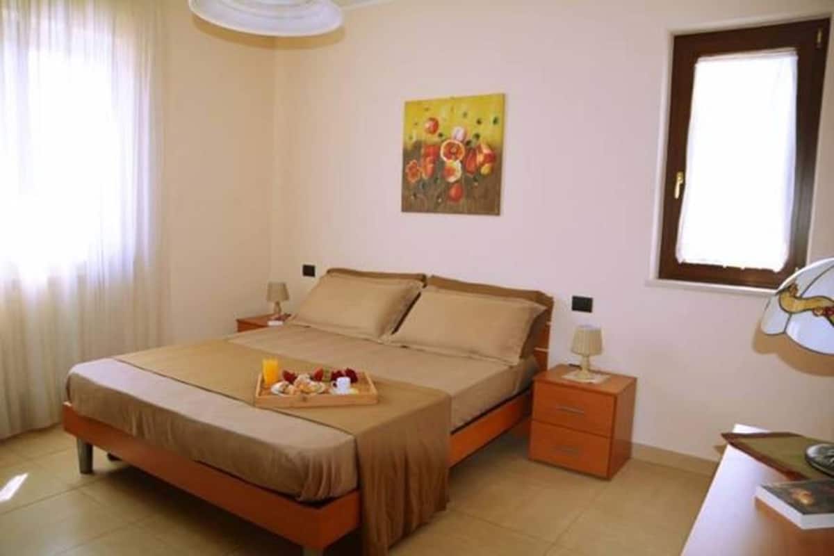 Une chambre à coucher bien rangée, avec un lit, des tables de chevet, un plateau contenant des aliments pour le petit-déjeuner et un tableau accroché au mur.