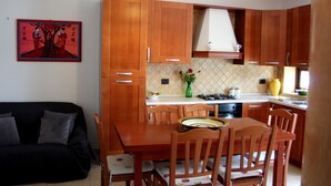 A modern kitchen with wooden cabinets, a dining table, and chairs. There is a vase with flowers on the counter. - B&B Atrium (Pompei)