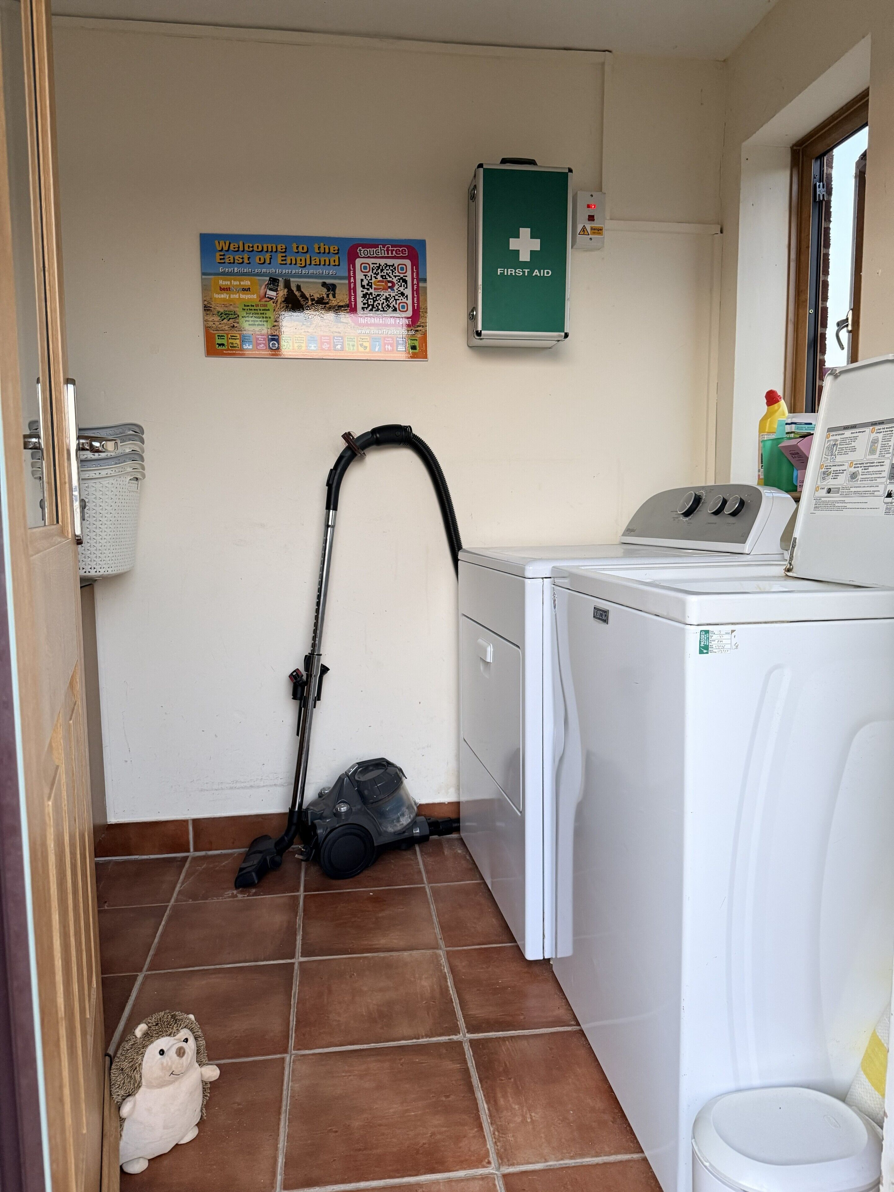 A laundry area with a washing machine, a vacuum cleaner, and a first aid kit on the wall.