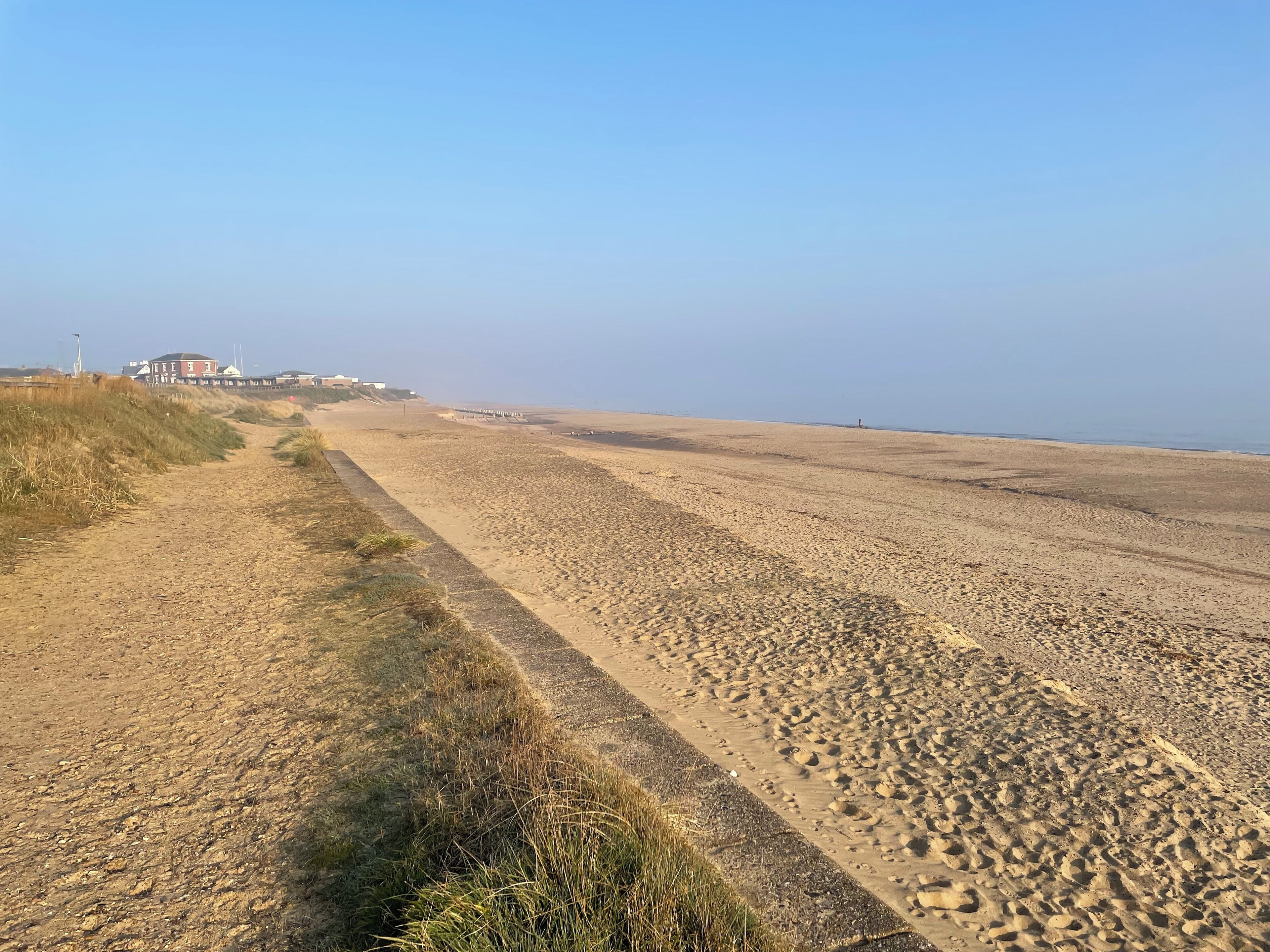 Ein sandiger Strand mit einem Weg zu einem Gebäude mit rotem Dach.