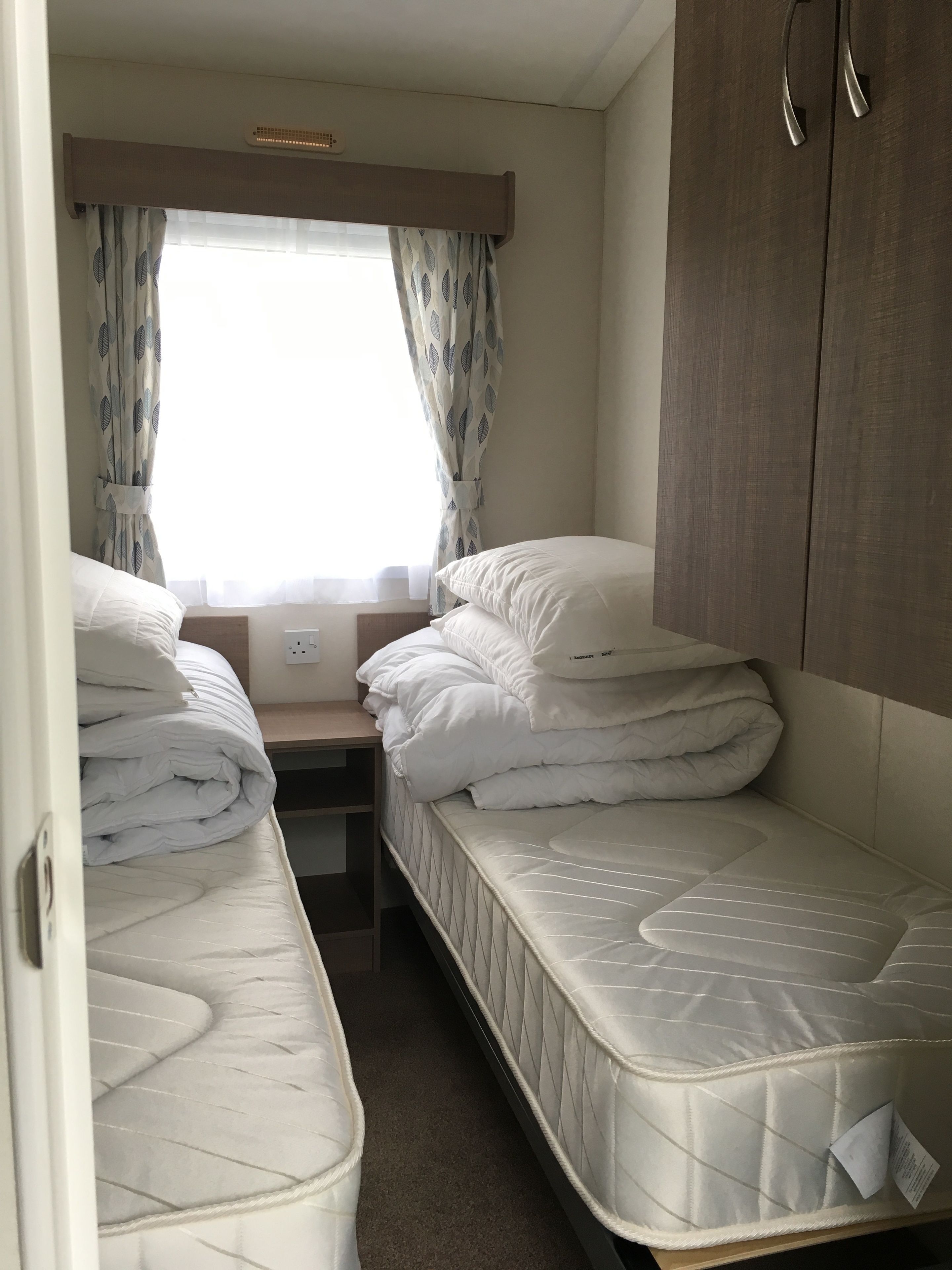 A compact bedroom with two single beds, a small table, and a wardrobe.