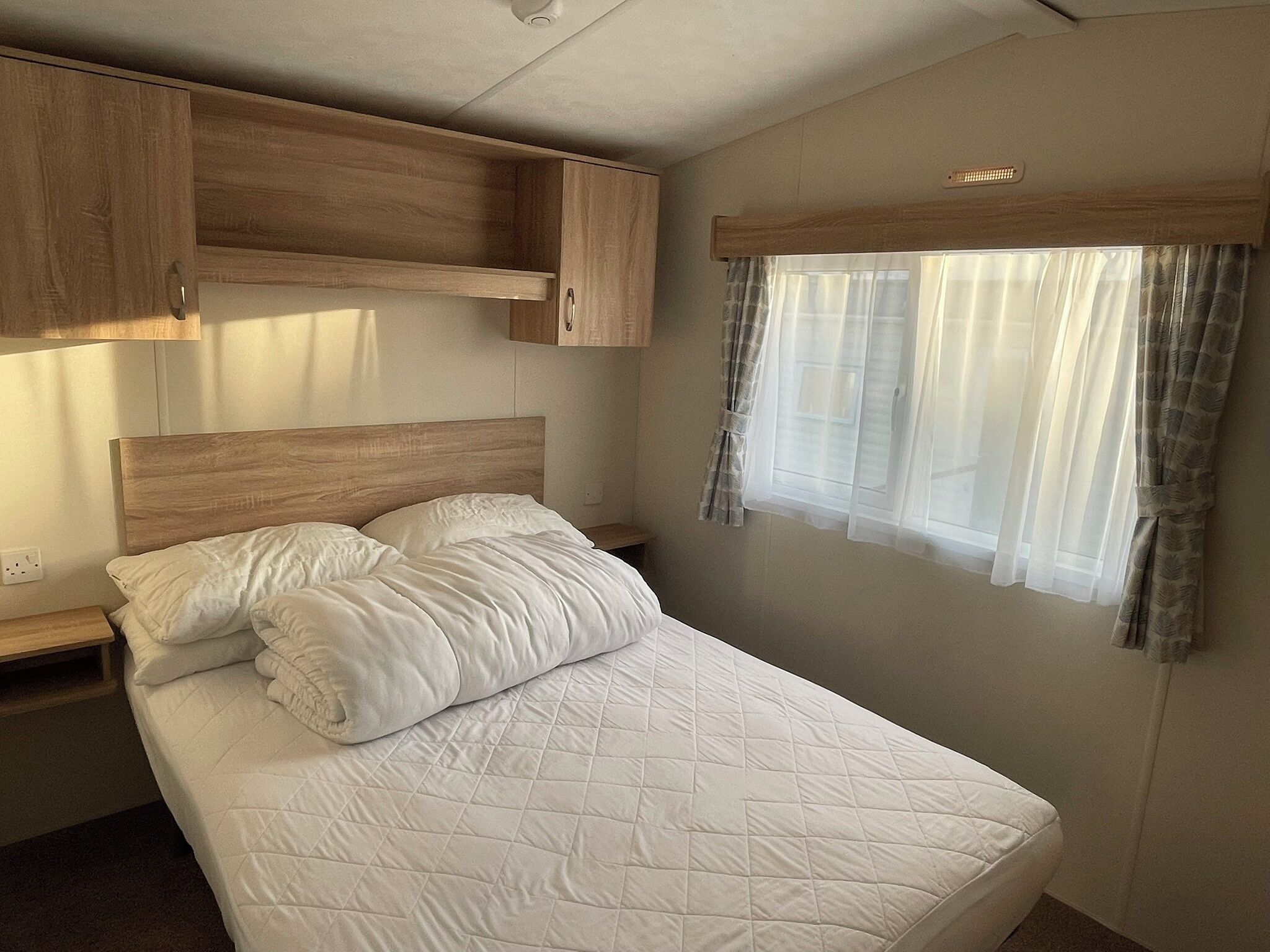A bedroom with a bed, wooden headboard, bedside tables, and a window with curtains.