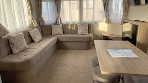 A cozy living area with a sofa set, a wooden table, and a television. - The Leas Beach Park (Norwich)