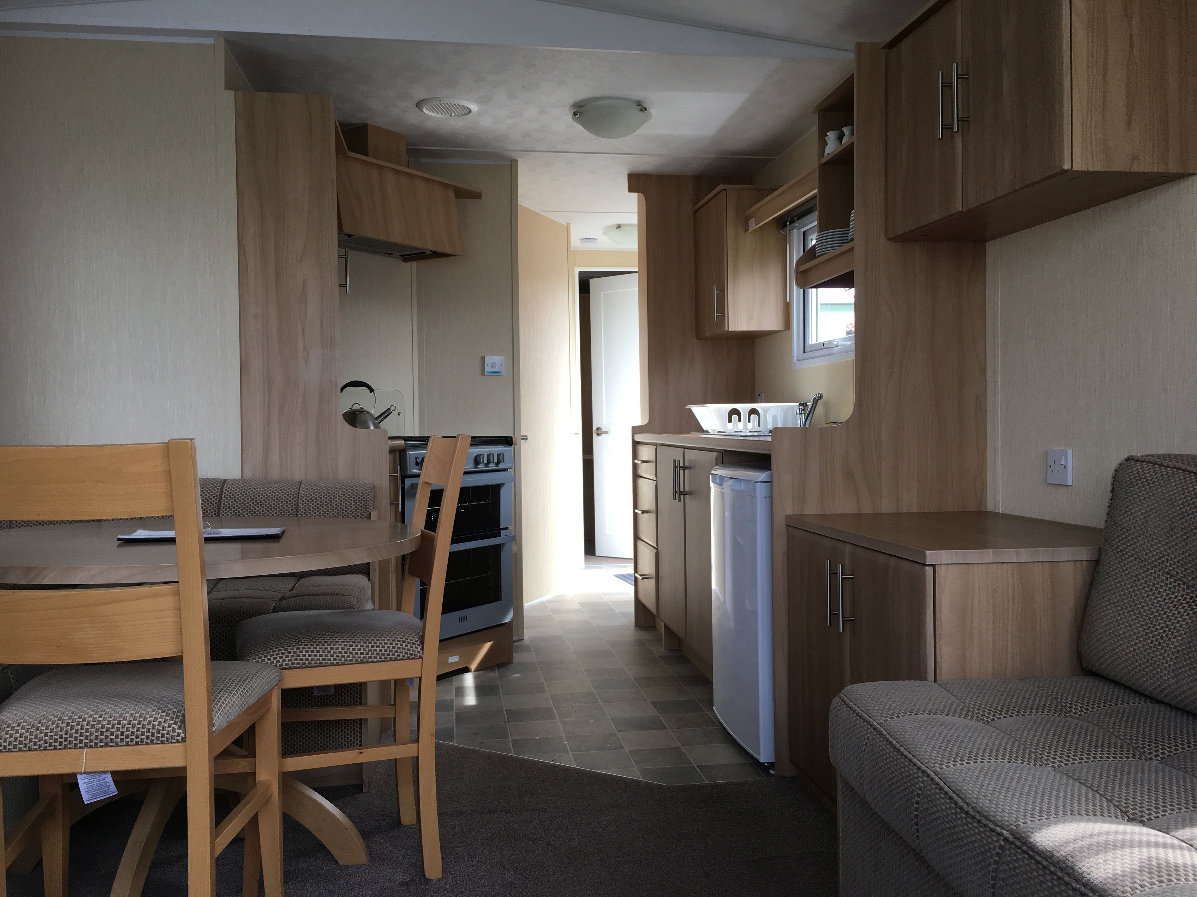 A compact kitchenette with a stove, oven, and dishwasher. There is a dining table with chairs and a sofa.