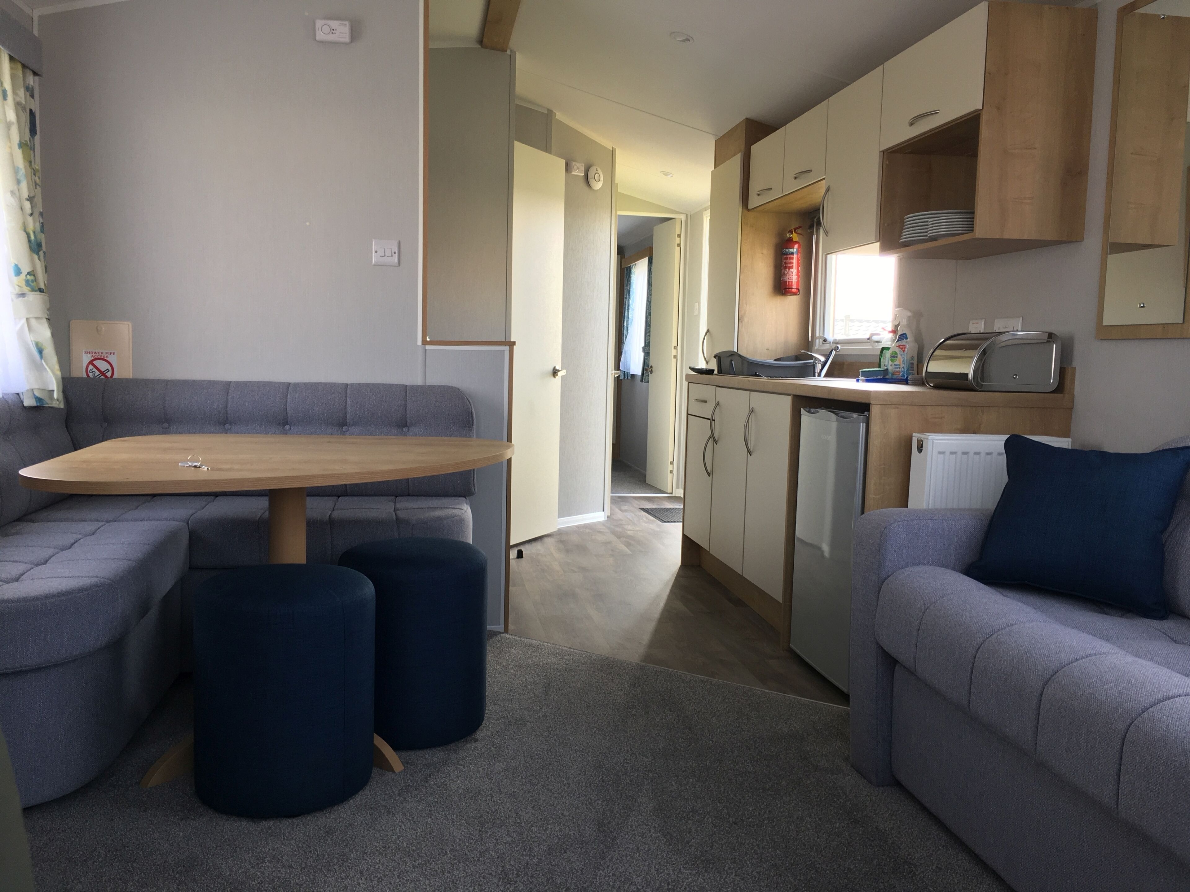 Ett kompakt bostadsutrymme med ett matbord, två soffor, en köksdel och en synlig brandsläckare.