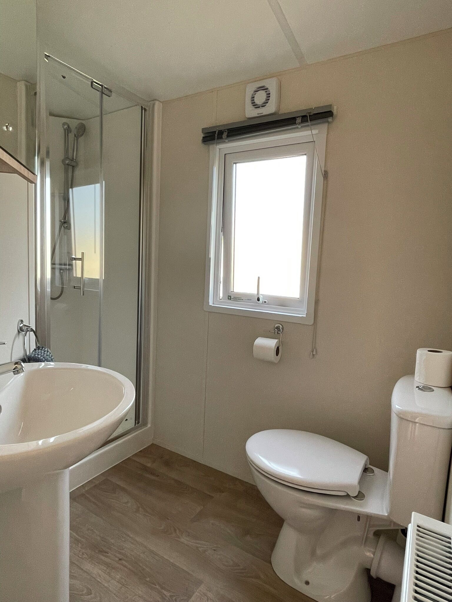 A bathroom with a shower, sink, toilet, and a window.