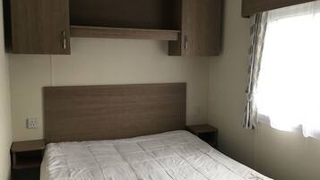 A bedroom with a wooden headboard, a white bedspread, and a window with curtains.