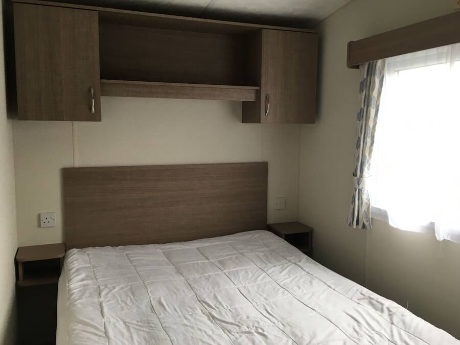 A bedroom with a wooden headboard, a white bedspread, and a window with curtains.