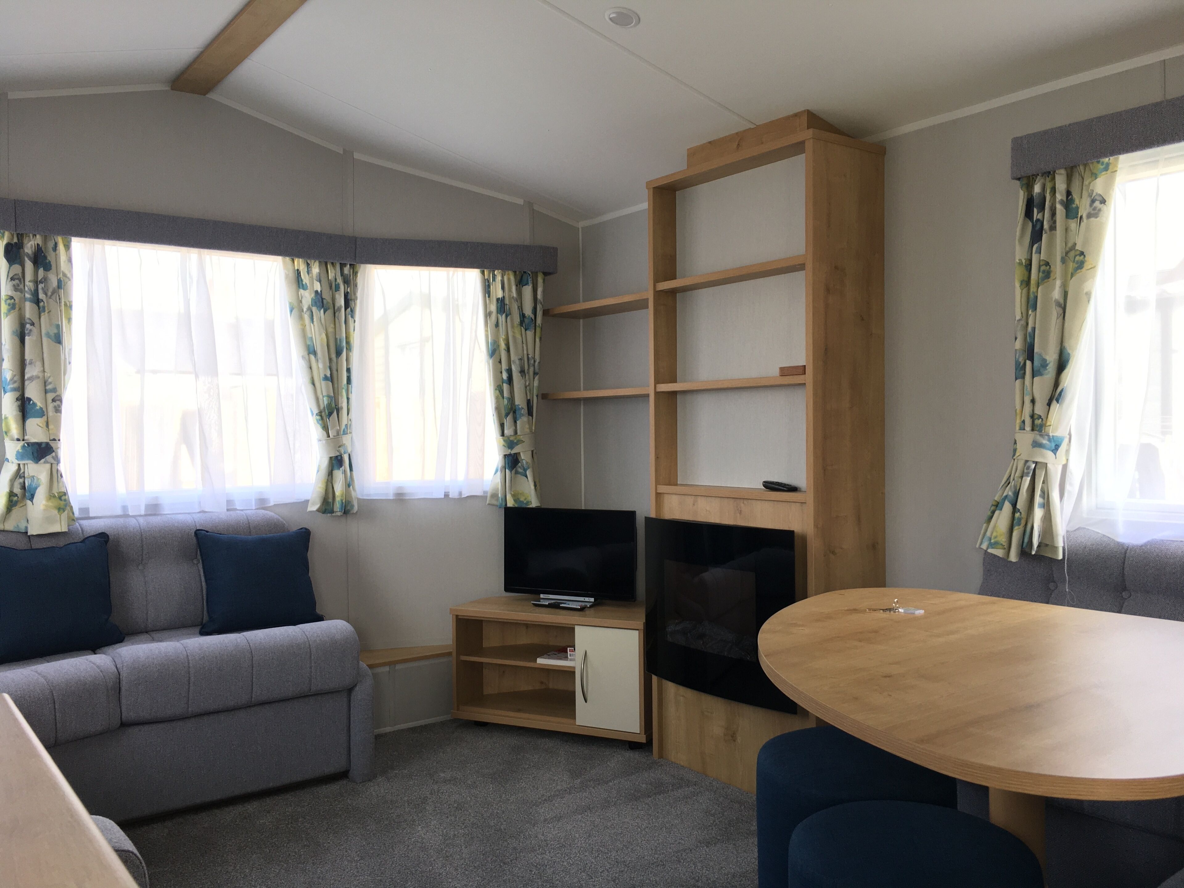 Een moderne kamer met een bank, een televisie, een houten boekenkast en een eettafel.