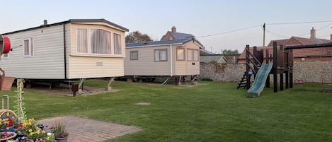 Residential area with a caravan and a small house, surrounded by a stone wall and lush greenery.
